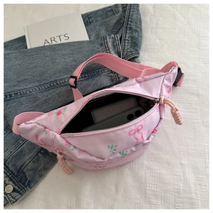 Detail of pink floral waist bag showing zip closure and adjustable strap on fabric background