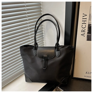 Dettaglio di una borsa tote nera capiente con chiusura a fibbia su sfondo minimalista