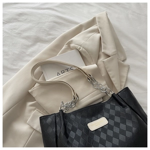 Detail of quilted texture and metal chain strap on a large black nylon tote bag