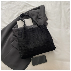 Détail d'un sac fourre-tout noir avec tissu gaufré et poignées tressées sur un blazer