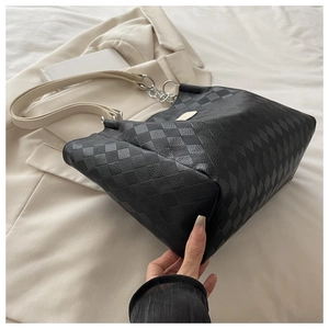 Detail of black quilted tote bag with cream strap and silver chain on beige blazer