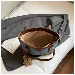 Top view of a denim tote bag with leather handles and a plush bear charm on a bed