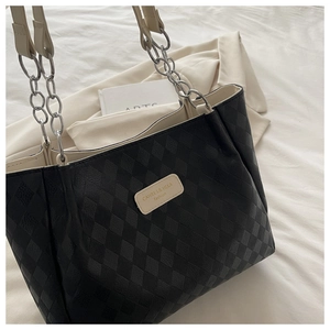 Close-up of diamond quilted black tote bag featuring beige leather logo tag and chain strap
