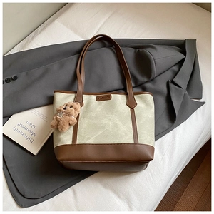 Detail of the green tote bag with brown leather trim and cute plush bear accessory