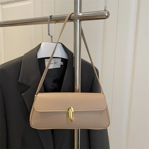 Minimalist beige leather underarm bag with gold metal clasp on a stylish suit background
