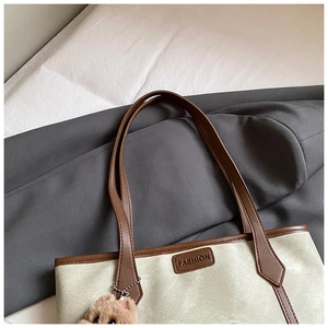 Detail of cream canvas tote bag with brown leather straps and plush toy charm