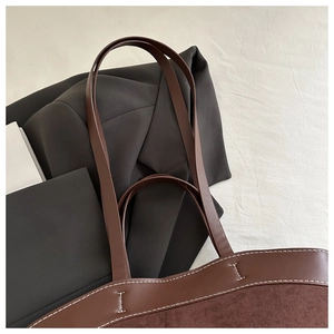 Close-up of deep brown tote bag showing leather handles and fine white stitching details