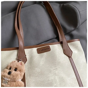 Detail of beige canvas tote with brown leather trim and a cute plush dog charm
