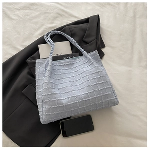 Détail d'un sac cabas bleu clair à texture gaufrée avec poignées tissées sur un costume