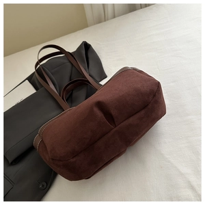 Detail of brown suede tote bag with leather straps and stitching on white bedding