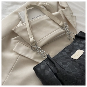 Detail of black quilted tote bag with chain strap and brand label on chic background