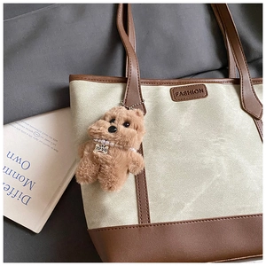 Detail of beige canvas tote bag with brown leather trim and plush dog keychain