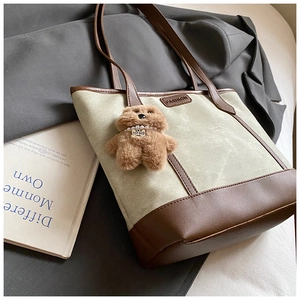 Detail of canvas tote bag with leather trim and brown plush bear charm accessory