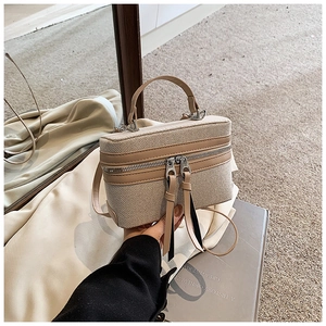 Detailed close-up of a boxy canvas handbag with contrast leather trim and dual zippers