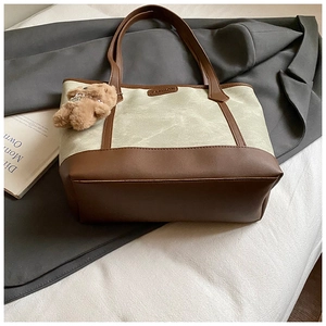 Detail of olive canvas tote bag with brown faux leather trim and plush bear charm