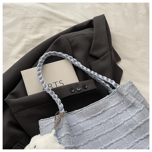 Détail du sac cabas en maille bleu clair avec un pompon blanc posé sur une veste grise