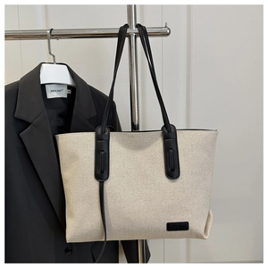 Detail of canvas tote bag with black leather handles and fashion logo patch