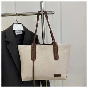 Detail of cream canvas tote bag with dark brown leather straps and fashion label tag