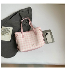 Fashionable pink checkered tote bag with leather handles shown in a stylish workspace