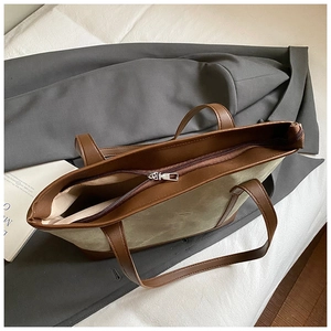 Detail view of large tote bag with zipper closure and brown leather handles in light green