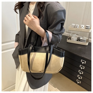 Detail view of stylish beige and black leather tote bag held by a model in a modern home