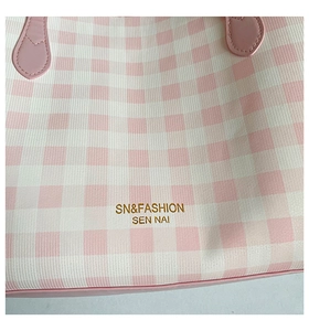 Detail of pink gingham tote bag with heart-shaped handle joints and gold lettering