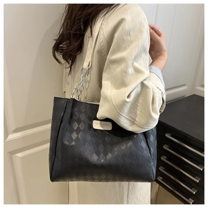 Detail of black quilted leather tote bag with silver chain strap and brand label
