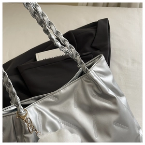 Detail of silver metallic tote with braided handle and plush cloud charm on bed