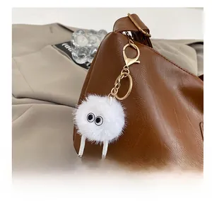 Close-up of white fuzzy ball charm with big cartoon eyes on a brown shoulder bag