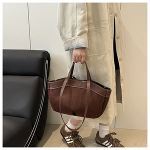 Detail of dark brown suede tote bag with contrast stitching on a beige trench coat