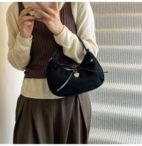 Detail of black suede hobo bag featuring leather bow and silver heart pendant charm