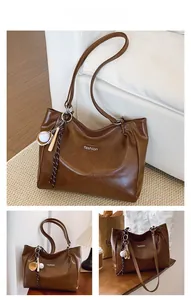 Close-up of brown PU leather tote bag with fashion logo and baseball charms on white sofa