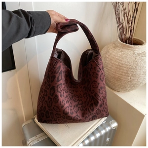 Detail of vintage leopard print tote bag in dark burgundy leaning on a suitcase