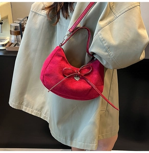 Detail of red suede crescent bag with leather bow and metallic heart pendant accessory
