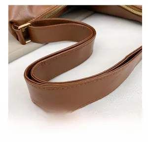 Detail of a brown leather dumpling bag featuring a wide adjustable strap with gold buckle