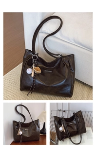 Detail of dark brown vintage tote bag with fashion tag and baseball charm on a white sofa