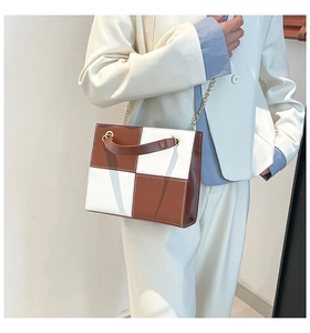 Détail d'un sac bandoulière à carreaux marron et blanc avec chaîne dorée sur mannequin