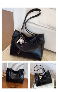 Detail view of large black leather tote bag with fashion label and baseball keychain