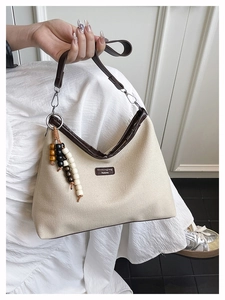 Detail of canvas bucket bag with brown leather trim and decorative wooden bead tassel