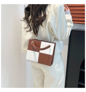 Modèle portant un grand sac à bandoulière en patchwork marron et blanc avec chaîne dorée chic
