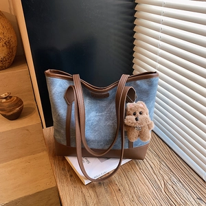 Blue denim and brown leather tote bag with a plush bear charm for daily commute fashion