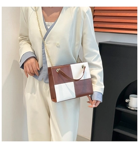 Détail du sac à bandoulière damier bicolore avec chaîne porté sur un blazer de couleur crème