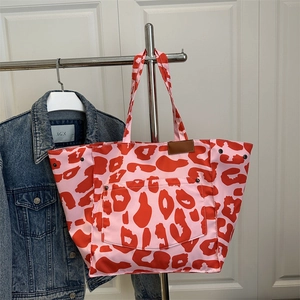 Pink leopard print canvas tote bag with red spots and front pocket hanging on a rack