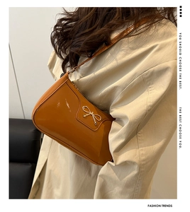 Close-up of caramel patent leather baguette bag with golden metal bow on a beige coat