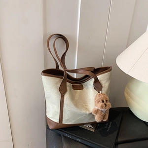 Canvas tote bag with leather trim, fashion label, and brown plush bear charm
