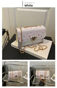 Close-up of white crossbody bag with pink floral cherry patterns and gold chain strap