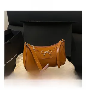 Detalle del bolso bajo el brazo de cuero PU brillante caramelo con lazo dorado y caja