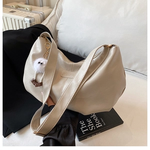 Detail der beigen Kunstledertasche mit breitem Gurt und Plüsch-Anhänger auf dem Sofa