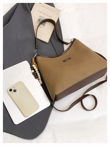Detail of vintage canvas tote with brown leather trim and wooden bead charm on a bed