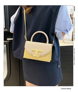Detail of yellow glossy leather crossbody bag featuring gold T-logo and glitter flap